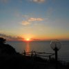 Tramonto sul mare con cielo nuvoloso, lampione a globo in primo piano.