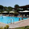 Piscina con persone, lettini e ombrelloni. Edificio sullo sfondo.