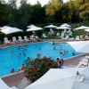 Una piscina affollata con lettini e ombrelloni bianchi. Alberi e vegetazione sullo sfondo.