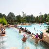 Persone in una piscina con scivolo e alberi circostanti.