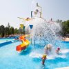 Bambini giocano in piscina con scivolo e spruzzi d'acqua.