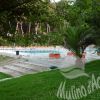 Area piscina circondata da alberi e ombrelloni bianchi.