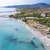 Spiaggia con sabbia chiara e mare cristallino, montagne sullo sfondo.