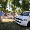 Un furgone bianco vicino a biciclette e panni stesi tra gli alberi.