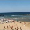 Spiaggia con ombrelloni, persone che giocano a pallavolo e mare calmo.