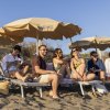 Persone sorridenti sedute sotto ombrelloni in spiaggia.