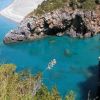 Una baia con acque turchesi, rocce imponenti e un promontorio coperto di vegetazione.