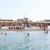 Spiaggia affollata con persone e file di ombrelloni colorati.