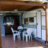 Un caravan con veranda coperta e sedie di plastica su una pavimentazione esterna.