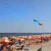Spiaggia con ombrelloni arancioni e aquiloni colorati nel cielo.