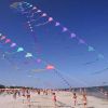 Spiaggia affollata con aquiloni multicolori volanti nel cielo azzurro.