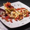 Calamari grigliati con pomodori e prezzemolo su un piatto bianco.