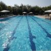Piscina vuota con strisce blu sul fondo, circondata da ombrelloni e lettini.