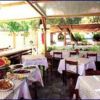 Ristorante all'aperto con tavoli apparecchiati e portate su un tavolo laterale.