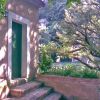 Edificio con porta verde, circondato da alberi e vegetazione.