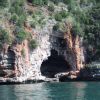 Una grande grotta rocciosa si apre sulla parete di una scogliera ricoperta di vegetazione.
