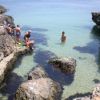 Bambini giocano e nuotano tra rocce vicino al mare trasparente.