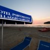 Spiaggia al tramonto con ombrellone e due lettini blu.