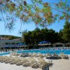 Piscina con lettini e ombrelloni, alberi sullo sfondo.