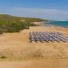 Spiaggia sabbiosa con file di ombrelloni blu, vicino a colline verdi.