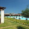Tavoli e sedie sotto una pergola vicino a una piscina. Area verde ben curata.