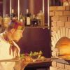 Cuoco che inforna una pizza in un forno a legna.