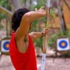 Persona intenta a tirare con l'arco in un'area con bersagli sfocati sullo sfondo.