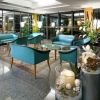 Salotto elegante con poltrone blu e tavoli, decorato con piante e candele.