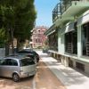 Auto parcheggiate accanto a un edificio verde con vetrate e tende. Alberi sul lato sinistro.