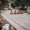 Pietraia con tavoli decorati e vasi di fiori, alberi e sedie sullo sfondo.