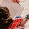 Persona legge un libro su sedia a sdraio in spiaggia.