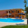 Piscina all'aperto con sdraio blu e ombrelloni, vicino a un edificio arancione.