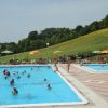 Due piscine con persone, colline e ombrelloni.