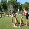 Due persone si allenano all'aperto in un parco, usando attrezzi ginnici in legno.
