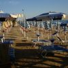 Spiaggia con ombrelloni blu e bianchi allineati su sabbia, lettini da sole vuoti.