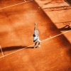 Giocatore di tennis serve su campo in terra rossa.