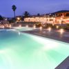 Piscina illuminata di notte con edifici sullo sfondo.