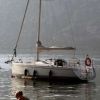 Una persona seduta vicino all'acqua, con una barca a vela ancorata dietro.