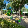 Un parco giochi con scivoli colorati e una giostrina, circondato da alberi verdi.