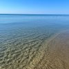 Una spiaggia con acqua limpida e calma, con onde leggere e cielo sereno.