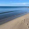 Spiaggia deserta con sabbia, mare calmo e orizzonte azzurro.