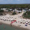 Vista aerea di una spiaggia affollata con ombrelloni e persone che nuotano.