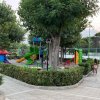Un parco giochi con scivoli verdi e strutture colorate, circondato da alberi e un vialetto.