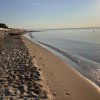 Una spiaggia al tramonto con mare calmo, sdraio bianche e un cielo limpido.