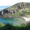 Piccola baia con spiaggia sabbiosa, circondata da colline rocciose e vegetazione.