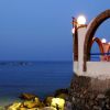 Terrazza con archi e sedie sul mare al tramonto, vista di barche e acqua.