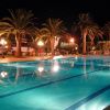 Piscina illuminata di notte con palme riflettenti in acqua.