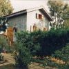Casa a due piani con giardino, circondata da alberi e cespugli.