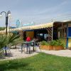 Esterno di una pizzeria con tavoli all'aperto, un'insegna blu e verde, e piante decorative.