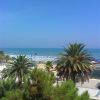 Vista di una spiaggia con palme e ombrelloni sotto un cielo blu.